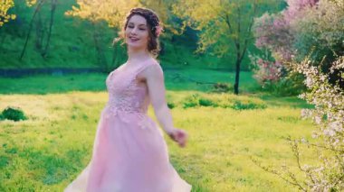 Mutlu gülümseyen kız modeli, arka planda dönen ağaçlara, açan pembe beyaz çiçeklere rüzgarın üzerine düşen yapraklara, ilkbahar yeşili çimenlere poz verir. Kıyafet dansı yapan kadın sağlık konsepti alerji yapmıyor..