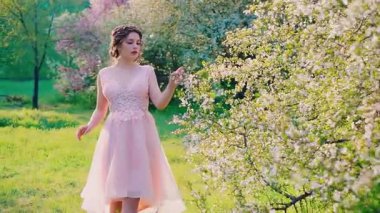 Şirin güzel kız yeşil çimen baharı bahçesinde çıplak ayakla yürüyor. Nazikçe çiçekli ağaçların eline dokunur. İyi istirahatler, güneşli günler. Esmer kadın, pembe zarif balo elbisesi. Gülen surat..