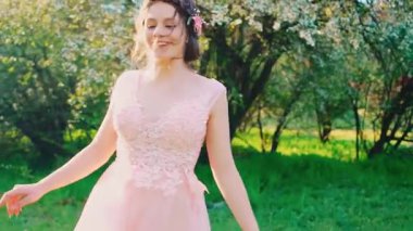 Şirin güzel kız yeşil çimlerin üzerinde çıplak ayakla yürüyor bahar bahçesinde çiçek açan ağaçlar. İyi danslar, dönüşler, iyi dinlenmeler. Pembe elbiseli esmer kadın. Gülümseyen yüz sağlığı kavramı alerjiden özgürlüktür.