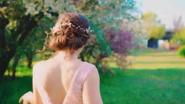 İlkbahar kırsal manzara parkı. Kadın yürür, arkasını döner, güzellik doğasının çiçek açan bahçesinden zevk alır. Esmer kız saçlara nazikçe dokunuyor, yaratıcı saç stili, beyaz sanat diyabeti. Pembe bayram zarif klasik elbisesi