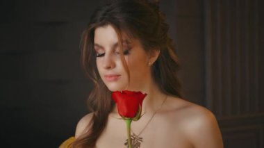 Genç fantezi kadın prenses portresi. Güzel kırmızı gül çiçeğini elinde tutan esmer bir kız. Altın takı kolyesi. Kapalı gözler. Çıplak omuzlar. Doğal makyaj, pembe dudaklar, ortaçağ saç stili.