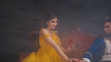 Antika koltukta oturan mutlu, romantik, evli çift. Cadılar Bayramı kostümü sarı klasik elbise, mavi smokin. Peri masalı prensi boynuzlu, kadın güzellik prensesi. Sisli sis odası dumanlı