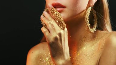 Güzellik mankeni kızların ağızlarına yakın çekim. Altın vücut derisi. Cazibeli altın renginde. Altın el, parmak sulu dudaklara dokunur. Güzel sanatsal makyaj, kadın yüzünde parlak boya. Leydi Tanrıça.