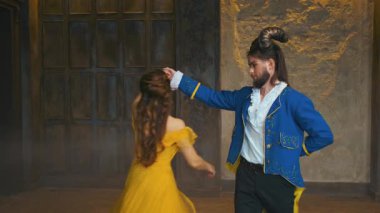 Ortaçağ balosunda romantik dans valsinde performans, fantezi karakterleri güzellik kadını ve erkek canavarı göster. Karnaval kostümlü, mavi smokinli, sarı, uzun, klasik elbiseli bir çift. Arkaplan eski tarz odası 