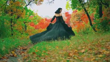 Kraliçe fantezi kadın mistik sonbahar sisli ormanında koşar. Turuncu kırmızı yeşil yapraklar. Korkak seksi gotik prenses kız dikiz aynasından bakıyor. Kraliyet vintage uzun ipek siyah elbise rüzgarda yavaş çekimde uçar.