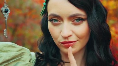 Sanat portresi fantezi kraliçesi gizli gümüş anahtarı elinde tutuyor dudaklarında işaret işareti sessizlik işareti. Sonbahar orman doğası. Güzel surat. Sarı yapraklar. Prenses kız. Klasik yeşil elbise..