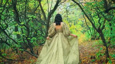 Kraliçe fantezi kadın mistik yaz aylarında ağaçlı sisli yeşil orman kemerinde yürüyor. Yeşillik gotik sis dumanı. Ortaçağ prensesi dikiz aynasından sarkık yeşil elbise kabarık kollu uzun ipek tren.