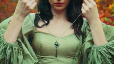 Sanat portresi fantezi kraliçesi elinde gümüş bir anahtar olan kadın boynuna zincirli bir kolye takıyor. Sonbahar orman doğası. Güzel surat. Sarı yapraklar. Prenses tanrıça seksi kız. Klasik yeşil elbise.