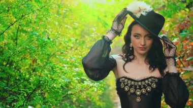 Sanat portresi fantezi kadın seksi bayan kraliçe siyah eski moda tüylü şapkalı. Manken pozu veren asil kız kameraya bakar. Güzel yüzlü eski moda duvak eldivenleri. yeşil doğa ağaçları güneş ışığı 4k