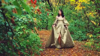 Kraliçe fantezi kadın mistik sonbahar ormanlarında yürüyor. Yeşil sarı turuncu yapraklar yola döküldü. Ortaçağ prenses kızı. Kraliyet vintage uzun yeşil elbise kabarık kollu. el dala dokunur.