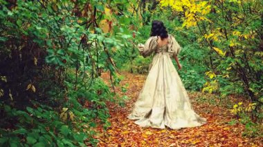 Kraliçe fantezi kadın mistik sonbahar ormanlarında yürüyor. Yeşil sarı turuncu yapraklar yola döküldü. Ortaçağ prensesi kızı dikiz aynasından bakıyor. Kraliyet mahsulü uzun açık yeşil elbise kabarık kollar.