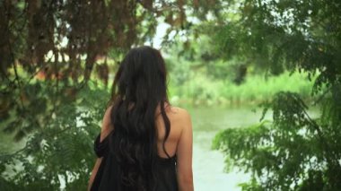 Uzun, zarif, ipek siyah elbiseli, gotik fantezi kraliçesi yağmur altında nehir kıyısında yürüyor. Gizemli kız portresi Prenses 'in dikiz aynasından geriye bakıyor. Yeşil ağaçlar yaz doğası. Bayan vampir.