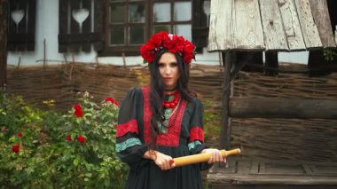 Elinde sopayla el ele tutuşmuş, kameraya tehditkar bakışlar atan Ukraynalı savaşçı bir kadının hayali portresi. Yaratıcı siyah ulusal elbise kırmızı boncuklar geleneksel çelenk gülleri gelincik çiçekleri. 4k