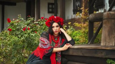 Yakın plan fantezi portresi üzgün kız ahşap kuyu evinin bahçesinde oturuyor. Otantik kadın güzellik suratı. Etnik klasik kostüm siyah elbise şık taç baş üstünde kırmızı çiçekler, gelincikler