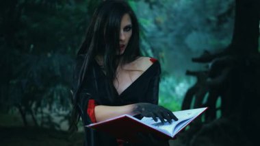 Uzun saçlı, fantezi kadın seksi cadı eski kitap okuma büyüsü tutuyor. Kız peri masalı gotik vampiri. Cadılar bayramı için koyu kırmızı elbise. Karanlık orman ağacı. Resim çizen eller.