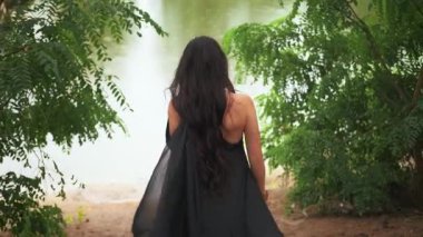 Uzun, zarif, ipek siyah elbiseli, gotik fantezi kraliçesi yağmur altında nehir kıyısında yürüyor. Gizemli kız portresi Prenses 'in dikiz aynasından geriye bakıyor. Yeşil ağaçlar yaz doğası. Bayan vampir.