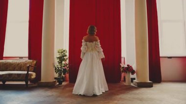 Seksi kraliçe kırmızı perdeleri açar, kenarlara atar, pencereyi açar ve yeni gün ışığının tadını çıkarır. Fantezi perisi bayan Mutlu kız sarı saç, beyaz eski moda elbise