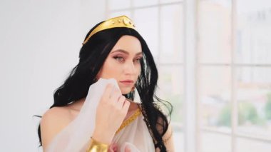 Fantezi Yunan tanrıçası kadın esmer, esmer, rüzgar esintisi içinde uçan, seksi gülümseyen yüz modeli. Seksi kız kraliçe. Beyaz stil ipek kumaş uzun sanat eseri yaratıcı elbise altın kaplama ağır çekim.