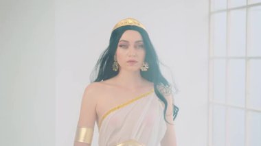 Fantezi portre güzelliği Yunan tanrıça kadın manken pozuyla karşılaşıyor. Afrodit kız seksi kraliçe. Beyaz, antika elbise, altın taç, siyah saç, rüzgârda uçuşan sinek. Stüdyo odası dumanlı..