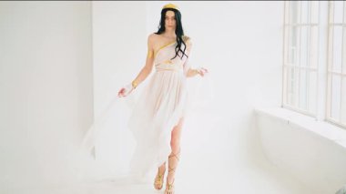 Fantezi resim sanatı Yunan tanrıçası esmer kadın yürüyen manken pozu. Afrodit kız seksi kraliçe. Beyaz stil ipek kumaş, uzun elbise, altın bilezikler, taç rüzgarda yavaş çekimde uçuyor. Bayan Elf.