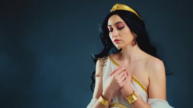 Fantezi sanat portresi parlak cilt güzelliği Yunan tanrıça kadın manken pozu verir. Afrodit kız seksi kraliçe. Beyaz elbiseli, altın kaplama, kumral, uzun saçlı, rüzgarda çırpınan sinek. Siyah stüdyo arka planı