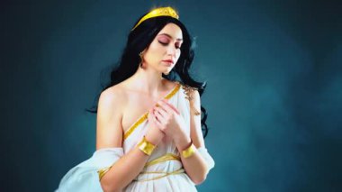 Fantezi sanatı Yunan tanrıçası esmer kadın manken pozu. Afrodit kız seksi kraliçe. Beyaz tarzı ipek kumaş uzun elbiseler altın bilezikler rüzgarda uçuşan taç sineği. Koyu mavi gökyüzü dumanı