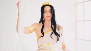 Fantezi Yunan tanrıçası el sallayan, gülen yüzlü kadın. Esmer manken pozu. Seksi kız kraliçe. Beyaz stil ipek kumaş uzun sanat eseri yaratıcı elbise altın taç. yavaş çekim