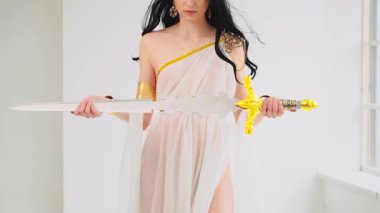 Yunan savaş tanrıçası Athena 'nın antik çelik kılıcı elinde tuttuğu fantezi portresi. Yaratıcı tasarım ipekten elbiseler yaratıcı elbise altın aksesuarlar klasik kostüm. Uzun saçlar rüzgarda uçuşuyor