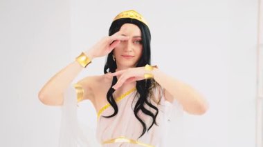 Fantezi Yunan tanrıçası el sallayan, gülen yüzlü kadın. Esmer manken pozu. Seksi kız kraliçe. Beyaz stil ipek kumaş uzun sanat eseri yaratıcı elbise altın taç. yavaş çekim