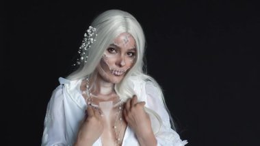 Santa Muerto, beyaz şenlikli bir elbise içindeki genç bakire, uzun sarı saçlı, karanlık bir odada büyüleyici bir ölüm tanrıçası, nazik bir görüntü ve gölgelerin canlandırılması, kırmızı parıltılı ölü bir kadın görüntüsü..