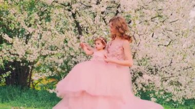 Güzel bir aile portresi. Genç, neşeli, mutlu bir kadın. Anne kucağında küçük bir kız çocuğu. Gülen surat. Aynı pembe, eski moda tatil gelinliği. Arkaplan baharı kiraz bahçesi, park