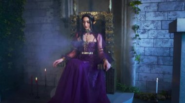 Sanat portresi fantezi kadın kötü elf kraliçe tahtta oturur, koyu mor uzun elbise. Seksi cadı elf kızı, sivri kulaklı. Gotik vampir prenses, altın taç. Eski tarz gece odası dumanlı.