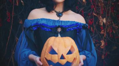 Cadılar Bayramı portakallı balkabağı feneri tutan kadın elleri. Güzel gotik kadın cadı ve Jack O Lantern. Seksi kız kırpılmış yüz. Mavi sisli sis bombası. Kadın klasik tatil kostümü..