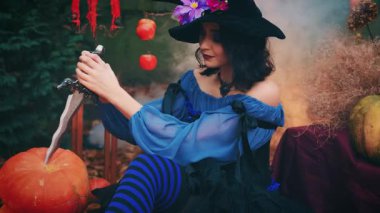 Portre fantezisi mutlu kadın cadı hançer bıçak tutuyor Cadılar bayramı için balkabağı oymaya hazır. Neşeli kız yaratıcı kostüm siyah mor külah şapka. Gülen yüz sanat makyajı. Sonbahar doğası