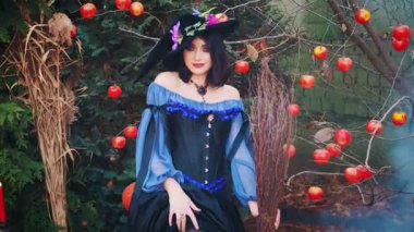 Mutlu ortaçağ fantezi kadını antik cadı kostümlü mor külah şapka. Gülümseyen seksi kız büyücünün elinde süpürge var. Cadılar Bayramı eğlence konsepti. Sonbahar doğa elma ağaçları portakal kabağı