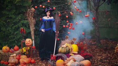 Cadılar Bayramı portresi mutlu fantezi kadın ellerinde süpürge tutuyor. Klasik mor kostümlü, ortaçağ elbiseli, uzun koni şapkalı, seksi poz veren büyücü kız. Sihirbaz kadın. sonbahar arkaplanı.