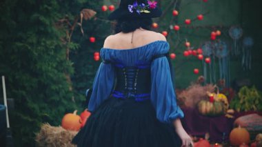 Fantezi kadın cadı kısa Midi kokteyl karnavalı şenlik mavi kabarık elbisesi ve kafasında şapkasıyla dolaşıyor. Siluet gizemli kız geri dikiz aynası. Cadılar Bayramı manzarası. Parlak sonbahar ağacı, turuncu balkabakları.