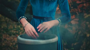 Gotik kadın, kadın cadı ellerinin yakın plan portresi. Sihirbaz kız sihirli kara uyanış yarattı. Parmakları antika fıçı kaynayarak büyülenir. Cadılar Bayramı konsepti. Mavi kadife elbise