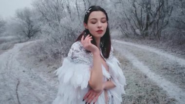 Beyaz karnaval düğün klasiği ortaçağ yaratıcı pelerinli güzel seksi kadın portresi. Parlak pırlanta elmaslar. Kuğu kuş tüyü. Esmer, gevşek saçlı. Kış buzlu orman arka planı