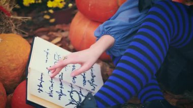 Portre mistik fantezi kadın cadı sihirli eski peri masalı büyü kitabı okur. fısıldayarak, el sallayarak, kız büyüsü yaparak. Mavi gotik kostüm siyah şapka. Arka plan Sonbahar Ormanı Sarı Turuncu Balkabağı