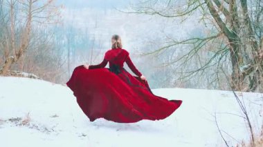 Dağ ellerinin tepesinde koşan mutlu, fantezi dolu bir kadın. Eski tarz kırmızı kumaş sinekler tren elbisesi rüzgarda sallanıyor. Kız kışın tadını çıkarıyor. Taze, soğuk, beyaz kar yağıyor. arka plan sanatı 4k