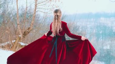 Fantezi portresi mutlu genç kadın dağın tepesinde duruyor etek tutan eller, rüzgarda uçan kırmızı kumaş. Prenses kız kış doğa dağlarının tadını çıkarıyor. Kar yağıyor. Kadın arkadan bakıyor. 4k