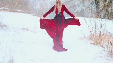 Dağın tepesinde koşan mutlu kadın elinde etek, elinde kırmızı kumaş rüzgarda dalgalanır. Prenses kız kışın tadını çıkarıyor. Soğuk, beyaz kar yağıyor. Kadın arkadan bakıyor. sanat 4k