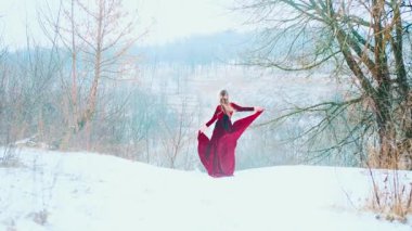 Dağın tepesinde dans eden mutlu bir kadın. Eteği elinde tutan, kırmızı kumaşı rüzgarda dalgalanan bir kadın. Prenses kız kışın tadını çıkarıyor. Taze, soğuk, beyaz kar. Arka taraftaki bayan sanat 4k