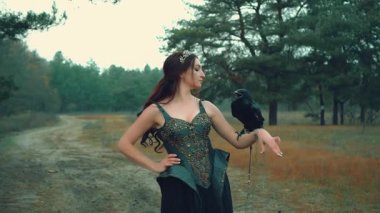 Ormanda kollarında kuşla seksi esmer, esmer bir kraliçe kadın. Kuzeye büyük kuzgunlara sevgi ve şefkatle bakıyor. Yaratıcı giysi fantazisi savaş tipi deri zırh nakışlı metal