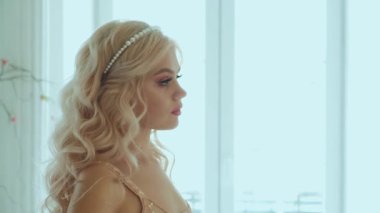 Yakın plan, güzel, üzgün, sevimli, çekici, seksi prenses kadın. Saç stili, kraliçe, uzun, dalgalı saçlar. İnci Tacı. Nazik doğal makyaj. Pembe dudaklar. Arkaplan içi klasik beyaz oda