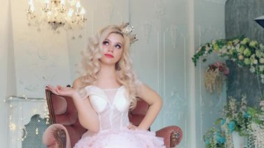 Ortaçağ koltuğunda oturan genç ve güzel bir kadın prenses boş alanda el hareketi gösteriyor. Sarı saçlar. Altın kraliyet tacı. Arka plan klasik kristal avize, beyaz odanın içi. Sevimli güzel yüz.