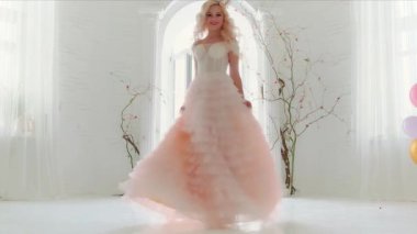 Klasik beyaz kraliyet odası renkli balonlarla dans eden genç ve güzel bir kadın. Gizemli bir şekilde büyüleyici gülümseyen yüz. Balo salonu havası zarif pembe elbiseler. Sarı sağlıklı uzun dalgalı saçlar, eski moda taç.