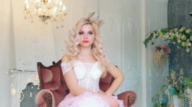 Genç, güzel, yaramaz kadın prenses sıkıldı, ortaçağ koltuğuna oturdu. Bayan fiske el serbest alan demek. Klasik kristal avize. Sarışın, uzun dalgalı saçlı kız. Zarif pembe balo elbisesi altın taç