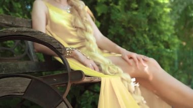 Gizemli bir kadının silueti, parlak sarı bir elbiseyle bankta oturuyor ve ince pürüzsüz bacaklarını altın bir bilezik ve parlak taşlarla şakayla sallıyor. Yüzsüz çekim.. 